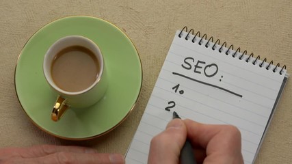 Wall Mural - SEO (search engine optimization) list - man hand writing a note with a black marker in a spiral notebook, overhead view