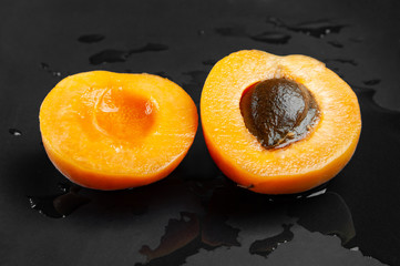 Top view of one sliced wet apricot on a wet dark background. Fresh juicy ruddy apricot on a dark clay plate splashed with drops of water.