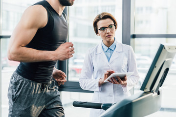 sportsman running on treadmill near doctor with Digital Tablet during endurance test in gym