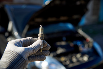 Wall Mural - Spark plug for engine in male hand on the background of a car with an open hood.