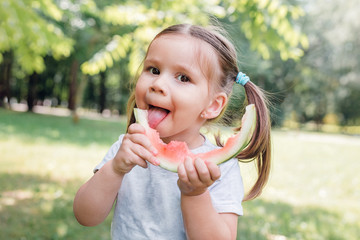 funny little girl eating watermelon in park in summertime