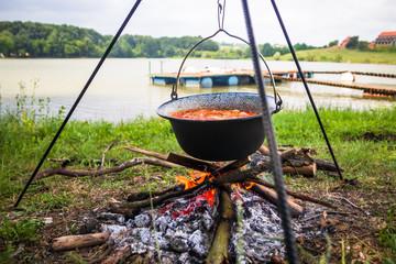 Cooking outdoor on a fire in a pot. Preparing  goulash in a nature by the lake.