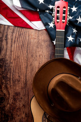 Fototapete - American culture, living on a ranch and country music concept theme with a cowboy hat, USA flag and acoustic guitar on a wooden background in a old saloon with copy space