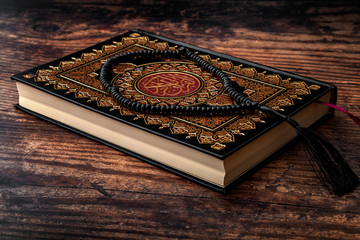 Worshiping God, reading the Quran and gaining knowledge and understanding from the holy text concept theme with a Koran and prayer beads isolated on wood background