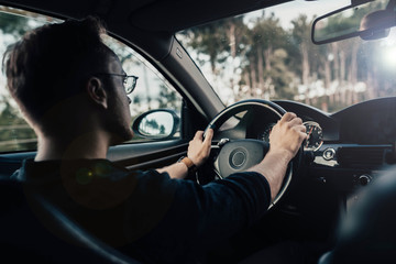 Wall Mural - driver with glasses drives a modern business car on a sunny day.