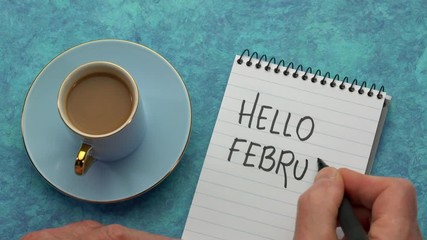 Canvas Print - hello febuary - a man hand writing a note with a black marker in a notebook, overhead view with a cu