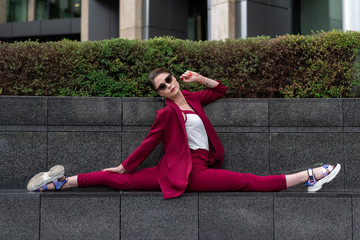 Women's business trouser suit in red. beautiful girl in glasses with a short haircut sat in the splits. girl gymnast conducts street workout.