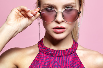 Wall Mural - Portrait of a smiling attractive young woman in tinted glasses on pink background