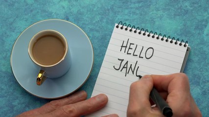 Canvas Print - hello january - a man hand writing a note with a black marker in a notebook, overhead view with a cu