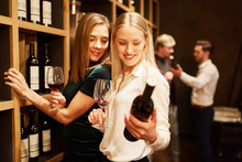 Two Young Women Are Looking At A Bottle Of Red Wine