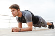 © Drobot Dean - Photo of masculine man in tracksuit doing plank while working out on wooden pier at seaside