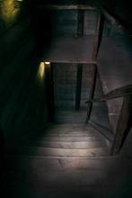 Darkness And Horror In A Ghostly Building. Inside On A Dark Wooden Staircase With Steps Down To The Basement Of An Old Abandoned House With Black Walls Mystical Light From A Dim Lamp On The Floor