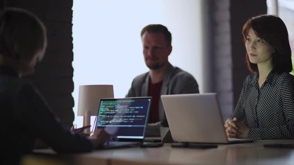 Team of four business people planning online startup at meeting. Focus on young Asian woman explaining his opinion. Female programmer coding on laptop