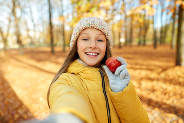 Poster - season and people concept - happy girl with apple taking selfie at autumn park