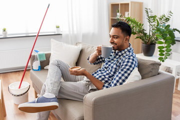 Sticker - household and people concept - smiling indian man drinking coffee and resting after home cleaning