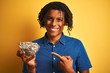 © Krakenimages.com - Afro american man with dreadlocks holding sunflowers seeds over isolated yellow background very happy pointing with hand and finger