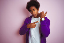 Young African American Man Wearing Purple Sweatshirt Standing Over Isolated Pink Background In Hurry Pointing To Watch Time, Impatience, Looking At The Camera With Relaxed Expression
