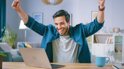 happy handsome man working on a laptop celebrates successful endeavor with yes gesture. freelances w