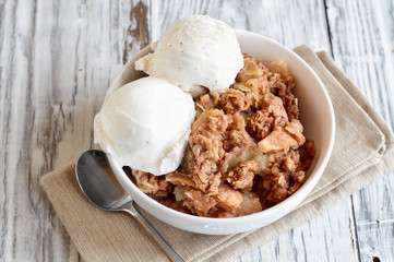 Wall Mural - Fresh hot homemade apple crisp or crumble with crunchy streusel topping topped with vanilla bean ice cream. Selective focus with blurred background. 