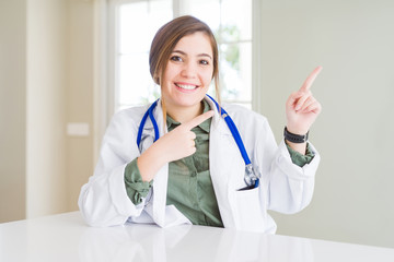 Sticker - Beautiful young doctor woman wearing medical coat and stethoscope smiling and looking at the camera pointing with two hands and fingers to the side.