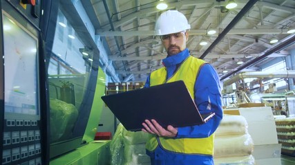 Male specialist is operating a laptop while standing near control panel