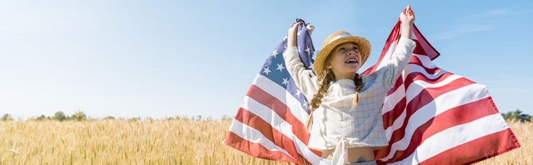 Poster - panoramic shot of happy child in straw hat holding american flag in golden field with wheat