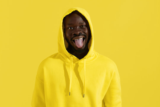 Black man in yellow hoodie making funny face on color background