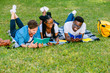 © Iryna - Handsome hipster man with african man and black woman students lying on a grass talking laughing reading books while doing homework at park in sunny meadow. Education and Friendship Concept.