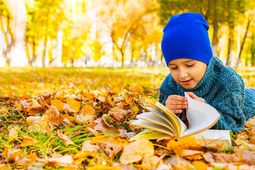 boy lying on his stomach reading a book in the fall in the Park