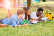 © Iryna - Group of multiethnic students lying on green grass at park, preparing for final exam, university education concept. Sun glare effect.