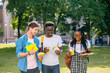 © Iryna - Group of three serious multiethnic students people coworkers talking, sharing ideas during lunch break standing outdoor university campus with books and backpacks. University education concept