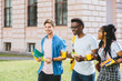 © Iryna - Group of three positive multiethnic students people coworkers talking, sharing ideas during lunch break standing outdoor university campus with books and backpacks. University education concept.
