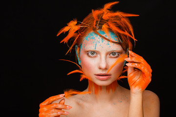 Portrait of a beautiful model with creative make-up and hairstyle using orange feathers