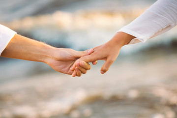 Crop shot of romantic couple holding hands on the beach.