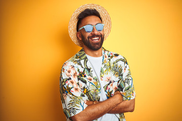 Wall Mural - Indian man on vacation wearing floral shirt hat sunglasses over isolated yellow background happy face smiling with crossed arms looking at the camera. Positive person.