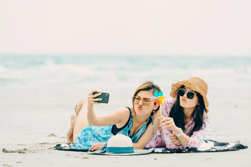 Two Women enjoying beach relaxing joyful in summer by tropical blue water.Model on travel wearing beach hat.