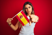 Young Beautiful Woman Holding Spanish Flag Over Red Isolated Background Pointing With Finger To The Camera And To You, Hand Sign, Positive And Confident Gesture From The Front