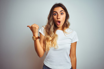 Young beautiful woman wearing casual white t-shirt over isolated background Surprised pointing with hand finger to the side, open mouth amazed expression.