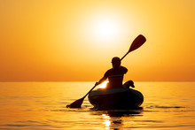 Red-haired Young Woman Is Rowing On An Inflatable Kayak By The Sea With A Dog Jack Russell Terrier On A Background Of Pink Sunrise In Beautiful Nature. Great Disk Of The Rising Sun. Sun Rays. Sport