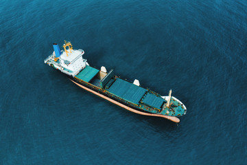 Aerial view of high-speed sea vessel for transportation of cargo vessel at high speed is drifting near the seaport of the city at sunset. Ship on the background of blue sea water. Import, export. Top