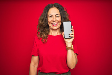 Wall Mural - middle age senior woman showing screen of smartphone over red isolated background with a happy face 