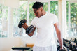 © twinsterphoto - Young African American man standing and lifting a dumbbell with the rack at gym. Male weight training person doing a biceps curl in fitness center