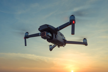 Wall Mural - Professional shooting drone flies in the air at low altitude against a blue sky and orange sunset. Drone makes photos. Modern new technology. Ready background with place for your text.