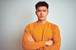 © Krakenimages.com - Young asian chinese man wearing orange sweater standing over isolated white background skeptic and nervous, disapproving expression on face with crossed arms. Negative person.
