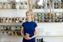 Portrait Of Woman Holding Jar In Front Of Spice Shelf In Kitchen