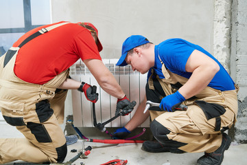 two plumber at work. Installing water heating radiator