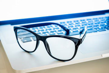 Computer goggles on a laptop, close-up view. Blue light blockers resting on computer keyboard, eye fatique problem concept