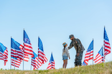 Wall Mural - selective focus of man in military uniform looking at daughter near american flags