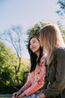 © Ramon Lopez/ADDICTIVE STOCK - Two multiracial young women in casual outfits talking and looking at each other while sitting on bench in park