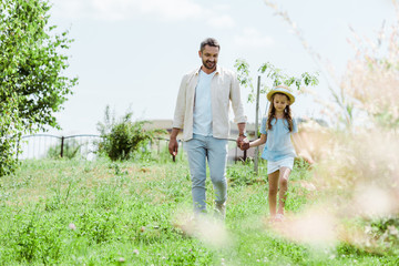 Wall Mural - selective focus of happy father and daughter walking near green plants and holding hands